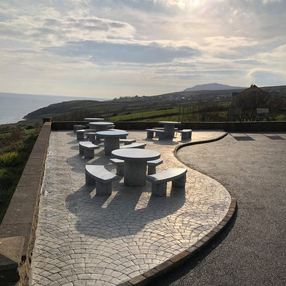 Outdoor seating area with Silver Granite round tables and benches on a stone patio overlooking a scenic landscape.