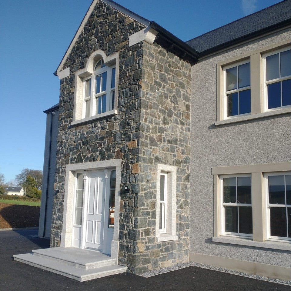 Stone house with a white door and windows on a clear day. Front porch features Silver Granite Window & Door Surrounds. 