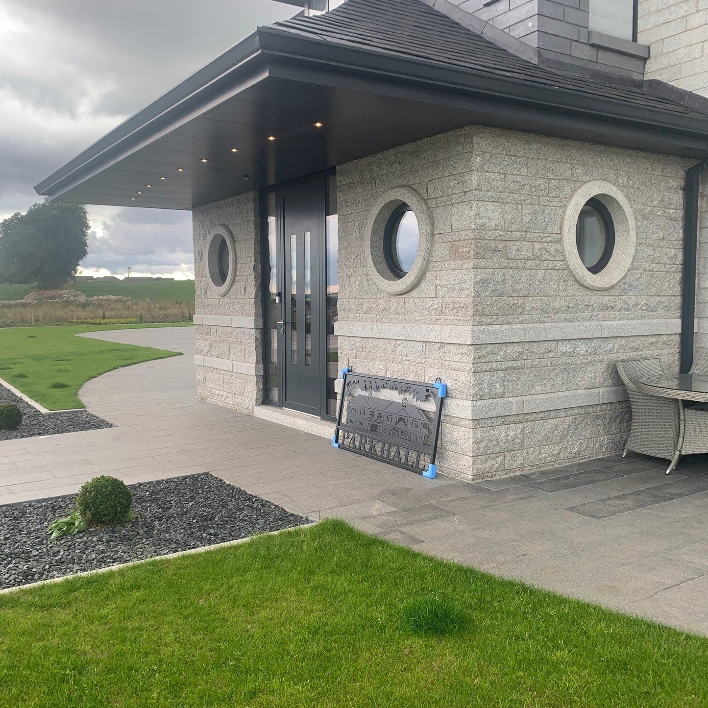 Modern building with circular granite window surround and a paved driveway leading to it.