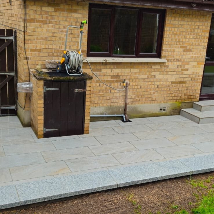Hose reel on a brick wall with a garden hose coiled up, outside a house. Patio is completed using Silver Quartz Diva Range Porcelain Paving. 
