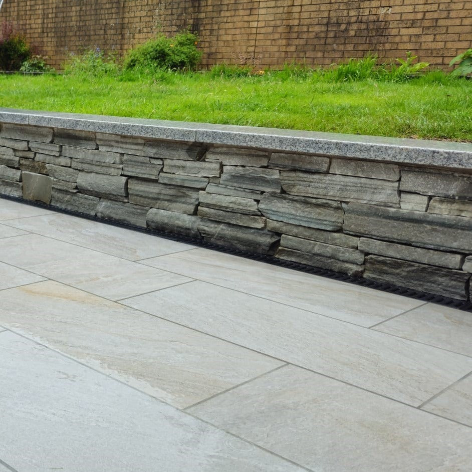Stone retaining wall with grass and porcelain tiles called Silver Quartz in the foreground.