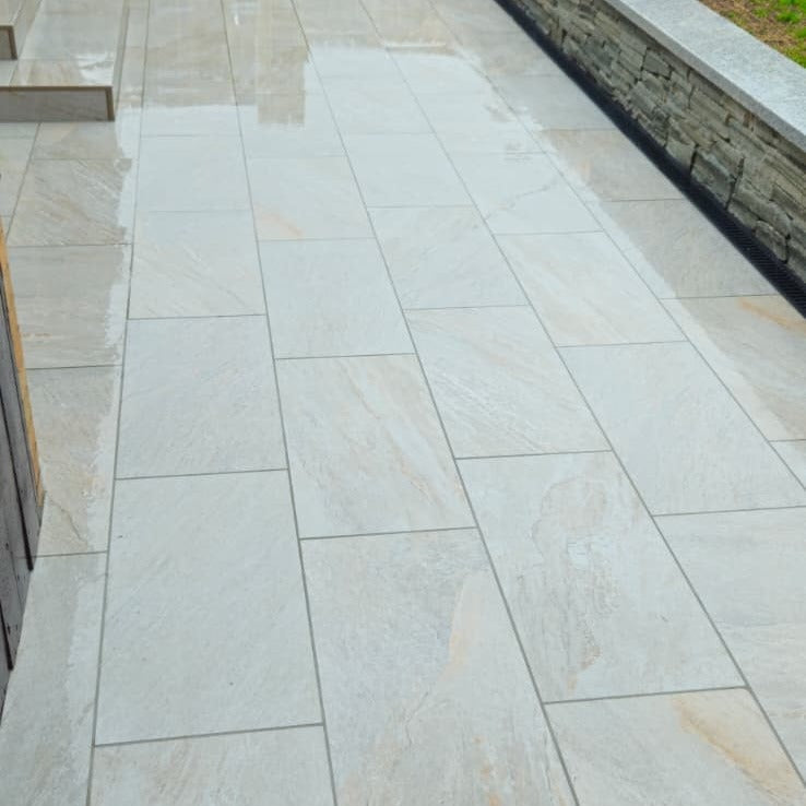 Silver Quartz Diva Range Porcelain Paving on a patio with a stone wall in the background