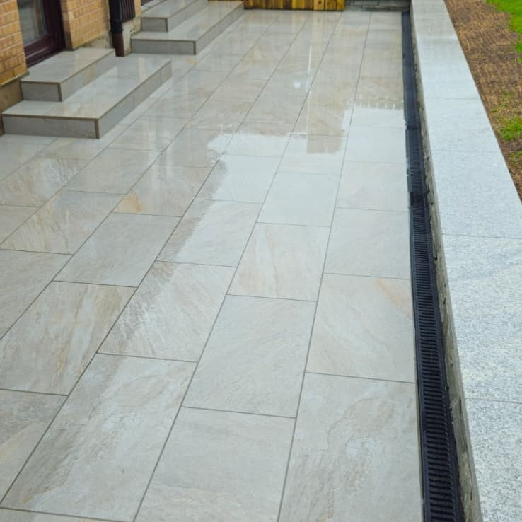 Outdoor patio with large stone tiles and a drain channel. Paving is Silver Quartz Diva Range Porcelain Paving Tiles. 