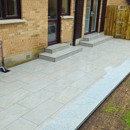 Paved patio area featuring Silver Quartz Diva Range Porcelain Paving Tiles leading to a brick building with steps.