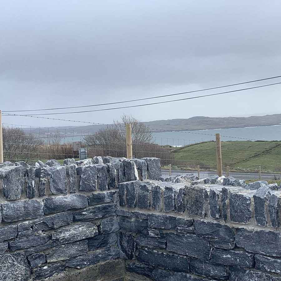 Low garden wall in Silver Shale walling stone overlooking a scenic view of fields and the sea. 