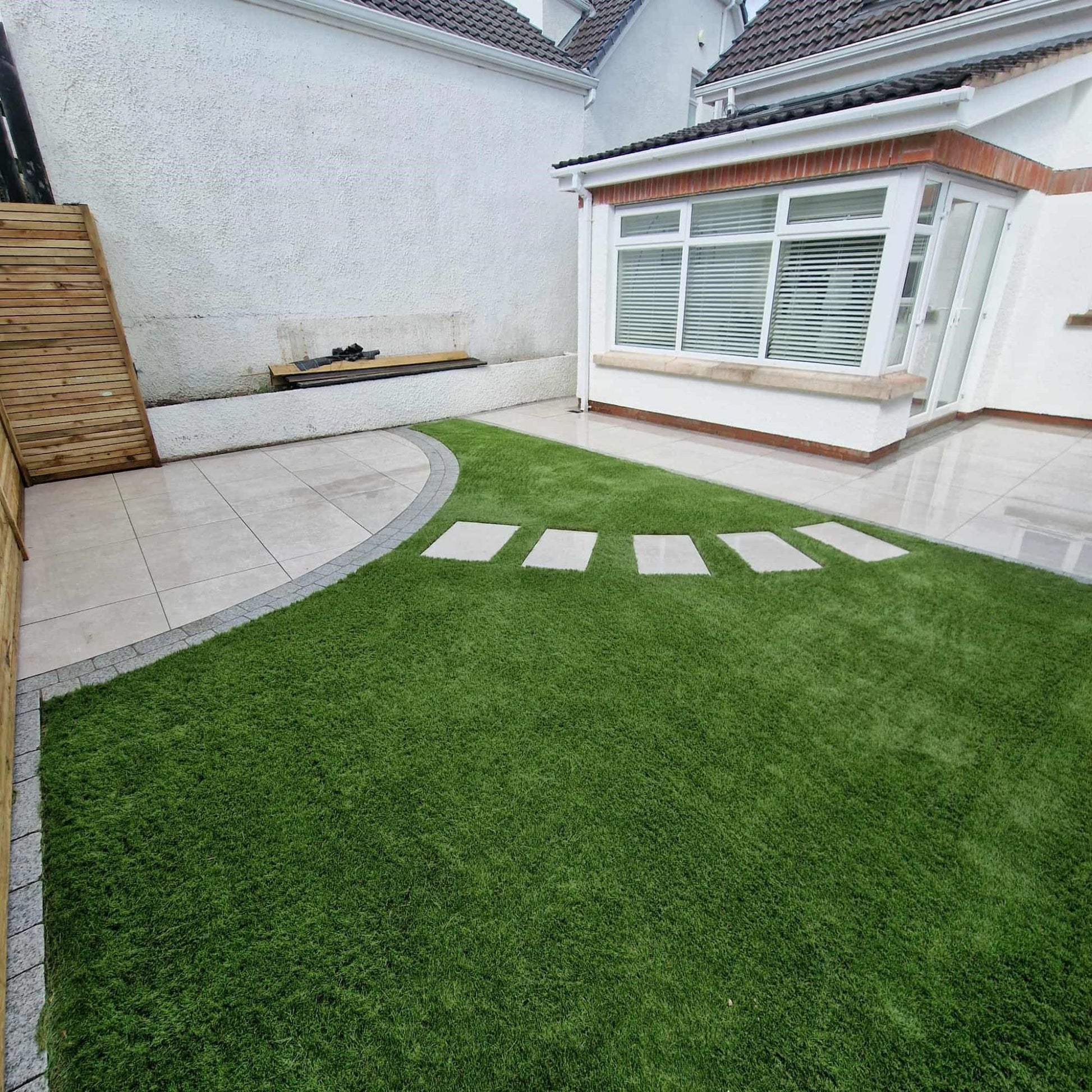 White house with circular patio area and stepping stones. Paving is Silver Street Range Porcelain Paving Tiles. 