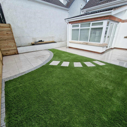 White house with circular patio area and stepping stones. Paving is Silver Street Range Porcelain Paving Tiles. 