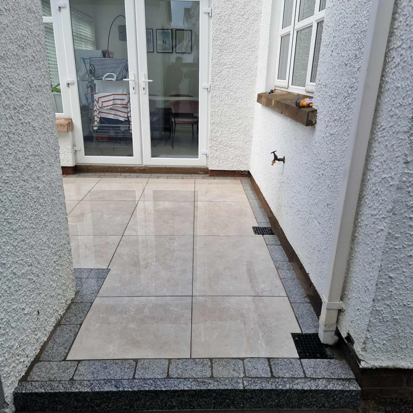 Outdoor patio area with tiled flooring and a glass door leading to a room inside a house. Paving is Silver Street Range Porcelain Paving Tiles. 