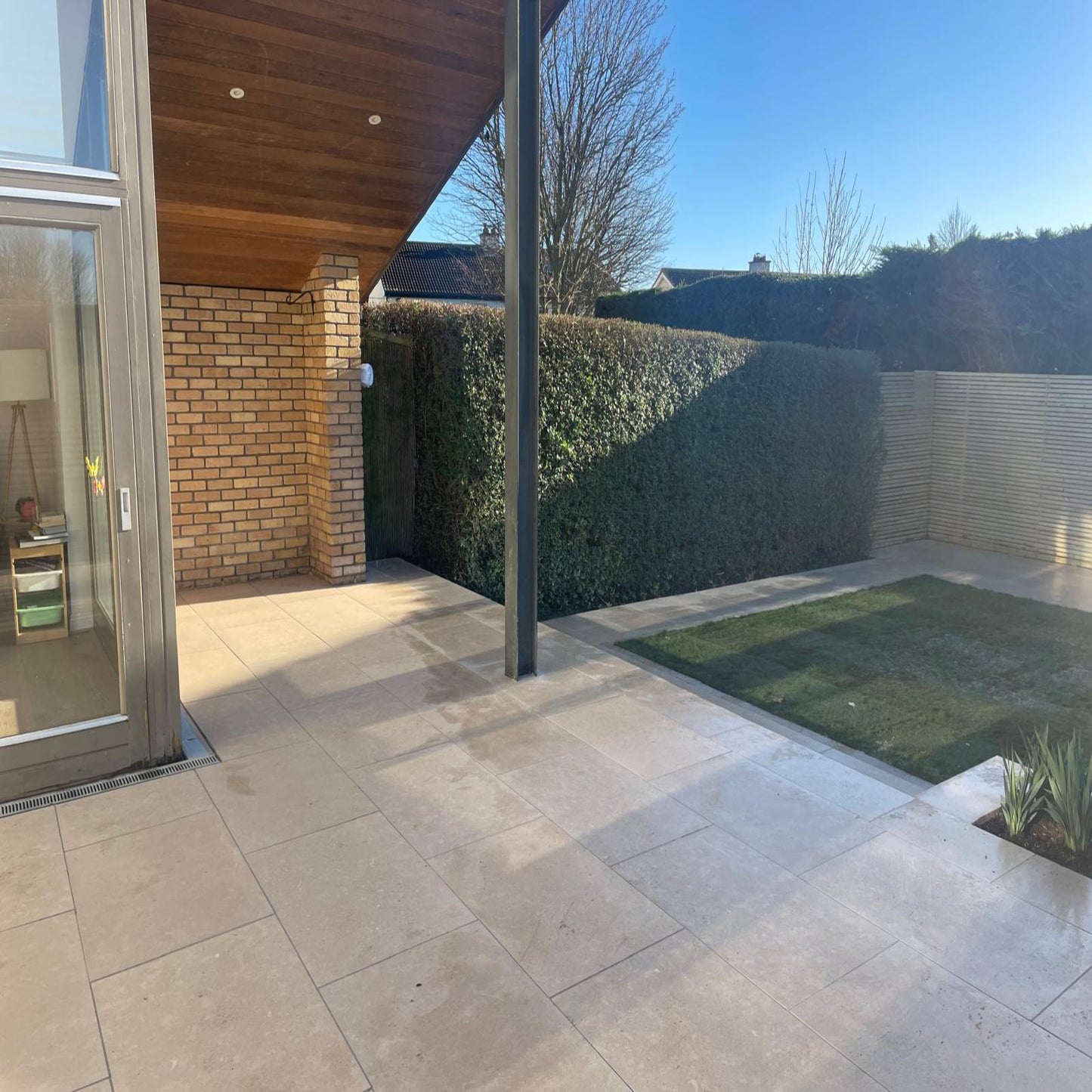 Modern outdoor patio area with a house and garden in the background. Paving is Sinai Pearl Porcelain Paving tiles.