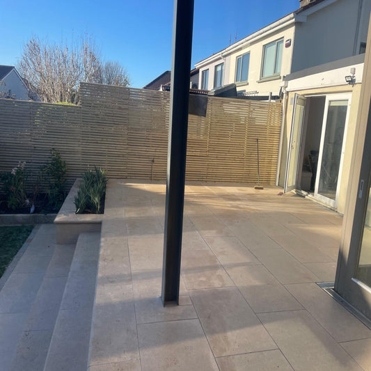 Patio area featuring Sinai Pearl Porcelain Paving tiles with a wooden fence and a modern house in the background. 