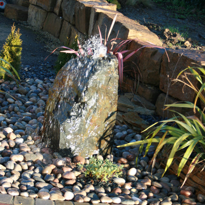 Small Slate Monolith drilled to create a water feature surrounded by pebbles and plants in a garden setting