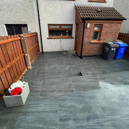 Patio area at the rear of a house surrounded by wooden fence. Paving is Smokey Jewel Range Porcelain Paving. 