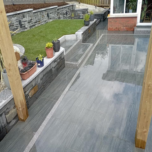 Outdoor patio area with stone tiles, garden beds, and potted plants. Paving is Smokey Jewel Range Porcelain Paving Tiles. 