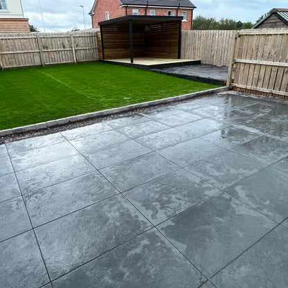 Paved patio area with grassy patch and wooden fence in the background. Paving is Station Black Jewel Range Porcelain Paving Tiles in 600 x 600 x 20mm size. 