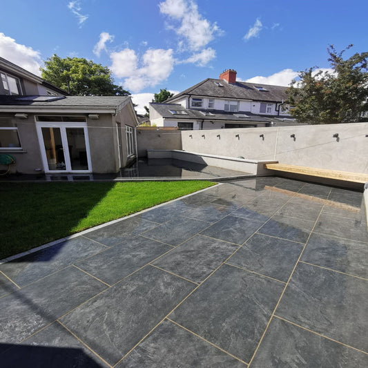An outdoor installation of Station Black porcelain paving in a garden setting, with a house and fence visible in the background.