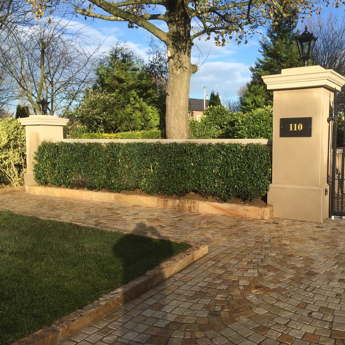 Large gate entrance with hedging and trees in the background. Tinted Mint Sandstone Kerbs were used along the driveway and boundary walls. 