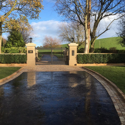 A tinted mint sandstone kerb on the edge of a garden, with trees in the background and a pathway leading to a gate.