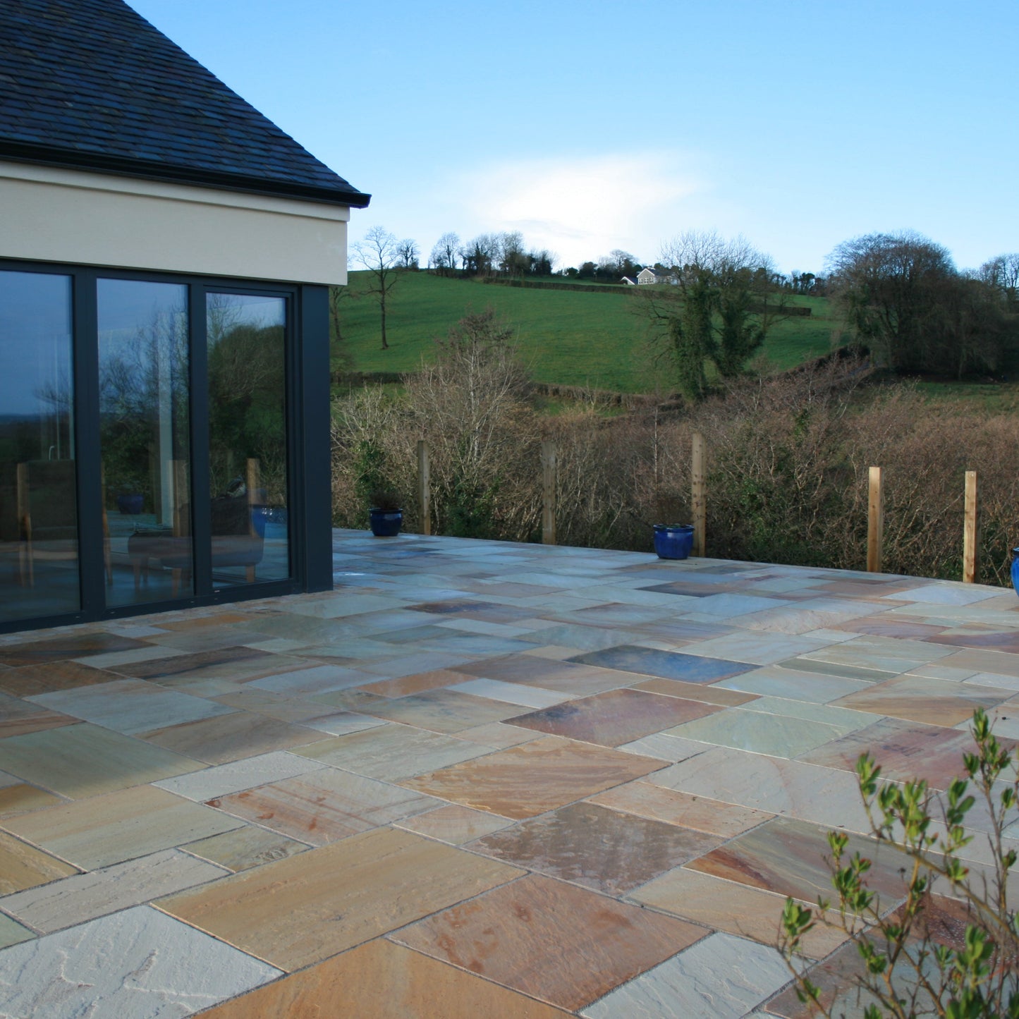 Modern house with large patio area featuring Tinted Mint Sandstone Paving in mixed sizes. 