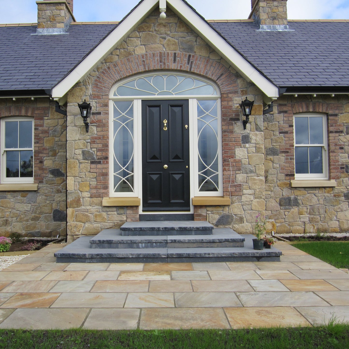 Stone house with dark stone steps leading down to a small paved area featuring Tinted Mint Sandstone. 