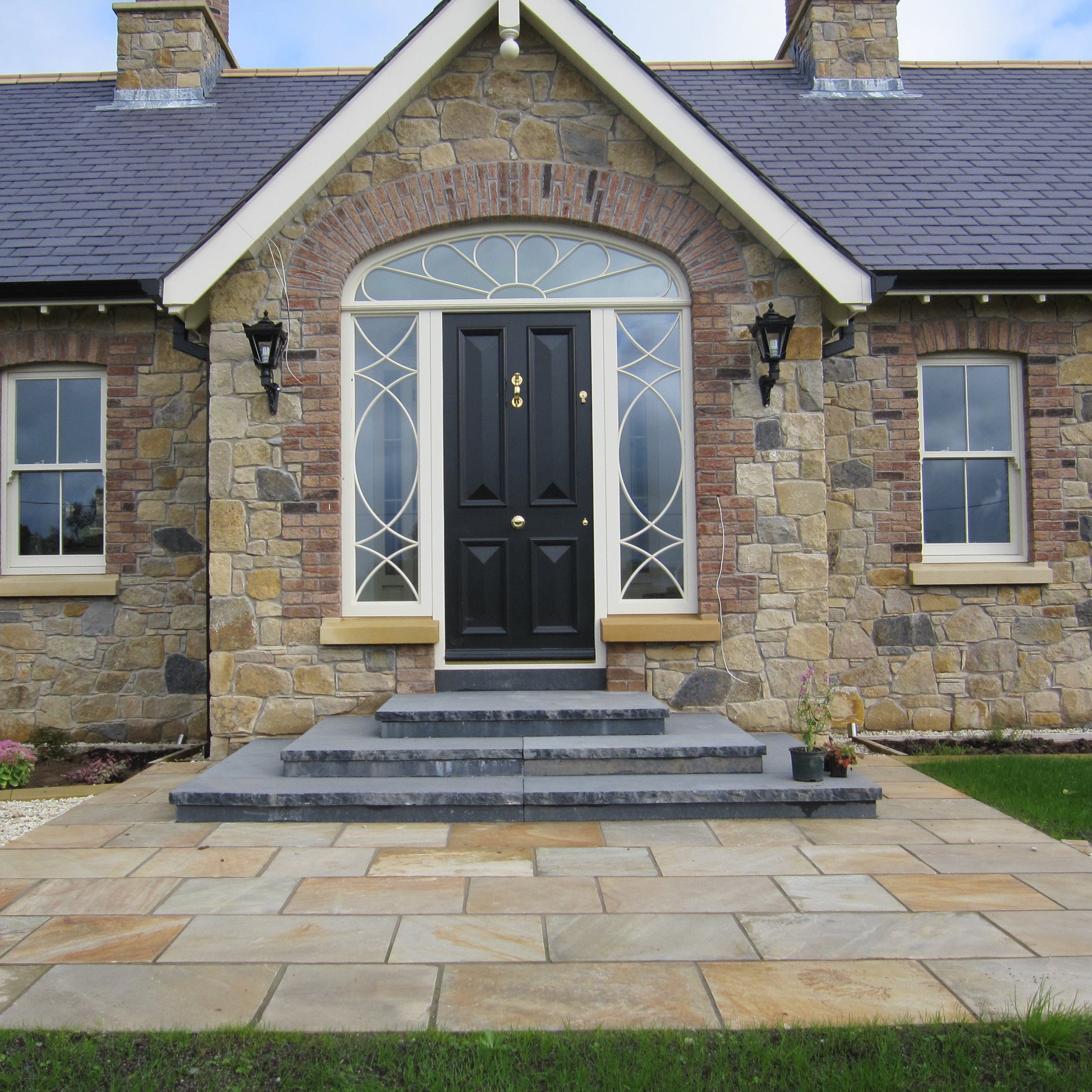 Stone house with dark stone steps leading down to a small paved area featuring Tinted Mint Sandstone. 