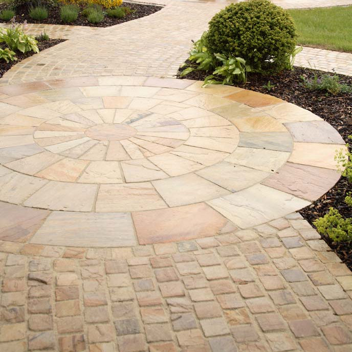 Pathway featuring 4m Tinted Mint Sandstone Paving Circle and matching Cobbles surrounded by planting and grass. 
