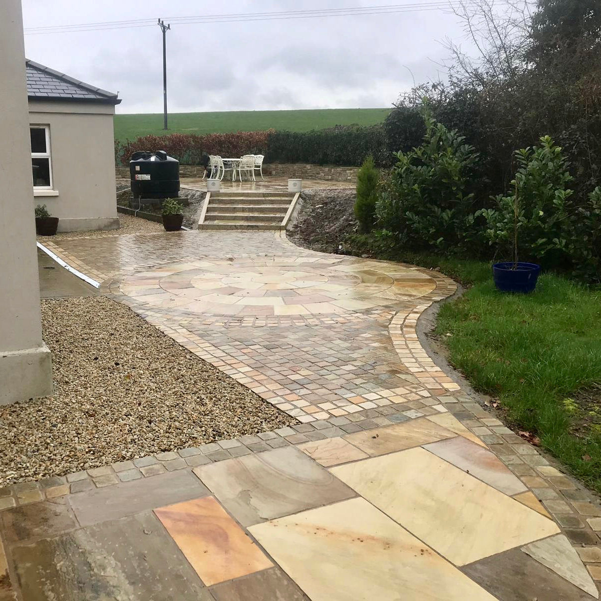 Pathway leading to seperate patio areas featuring a 4m Tinted Mint Sandstone Circle, Paving and Cobbles. 
