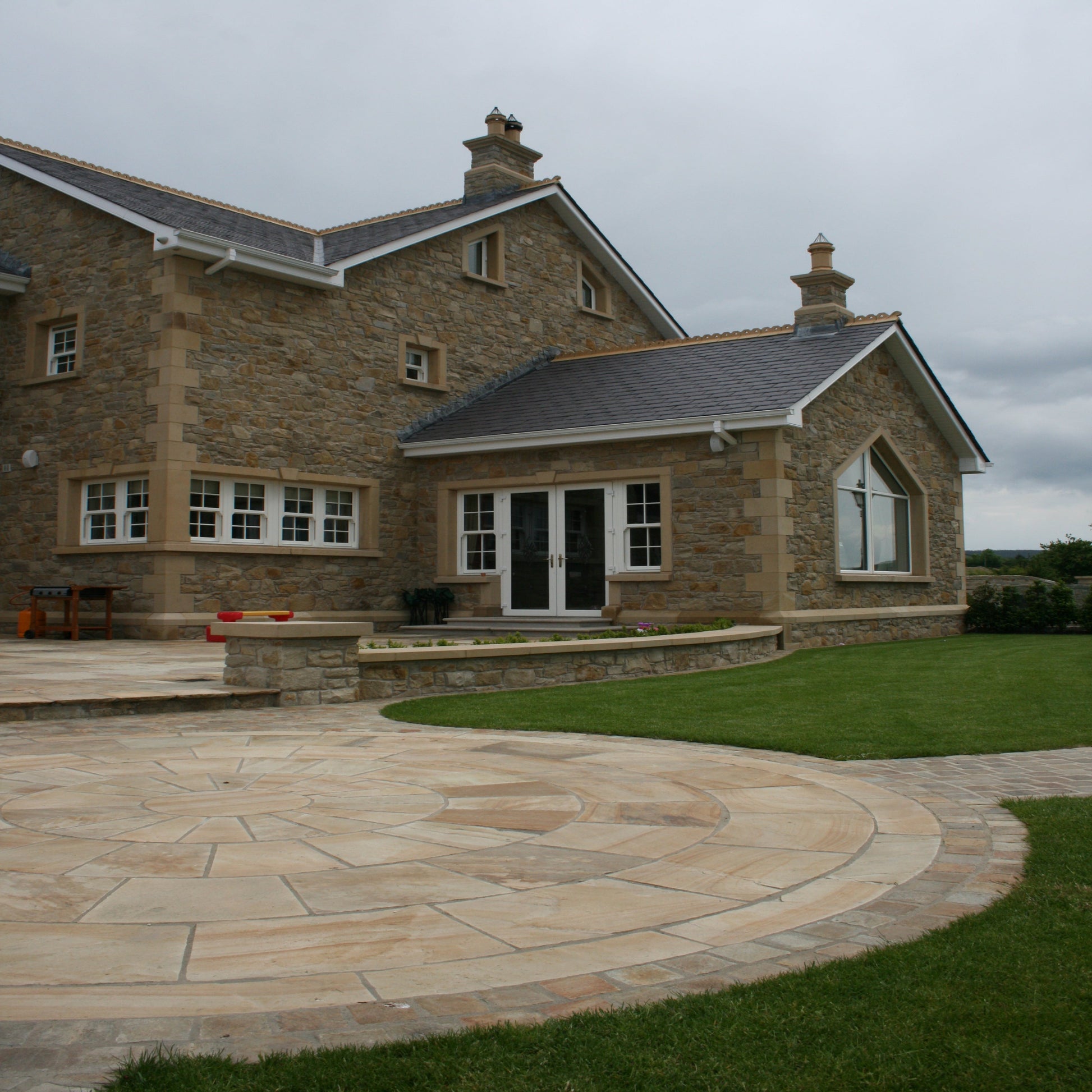 Large stone house with patio area featuring a 5m Tinted Mint Sandstone Paving Circle surrounded by Tinted Mint Sandstone Cobbles. 