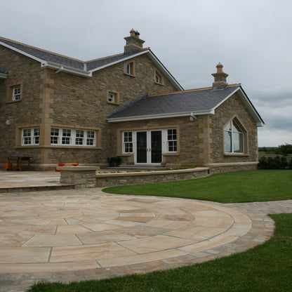 Large stone house with patio area featuring a 5m Tinted Mint Sandstone Paving Circle surrounded by Tinted Mint Sandstone Cobbles. 
