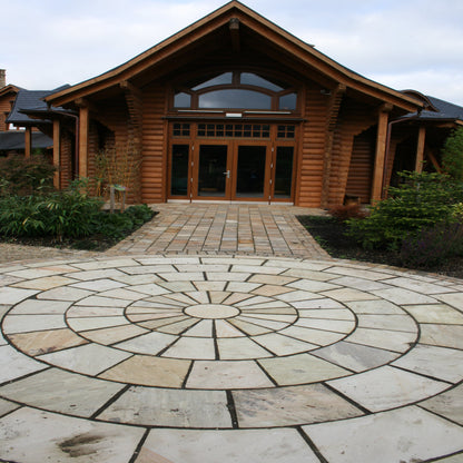 A 5m Tinted Mint Sandstone Paving Circle with pathway leading to large wooden building. 
