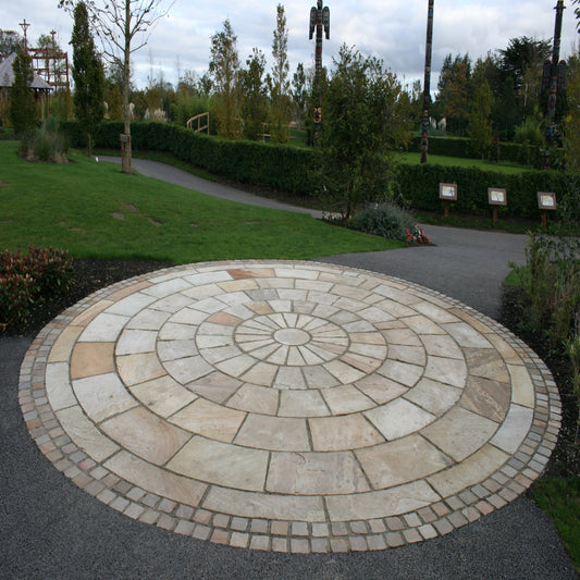 A circular pattern formed by Tinted Mint Sandstone Paving Circle set in an outdoor garden area, with a 5m diameter.