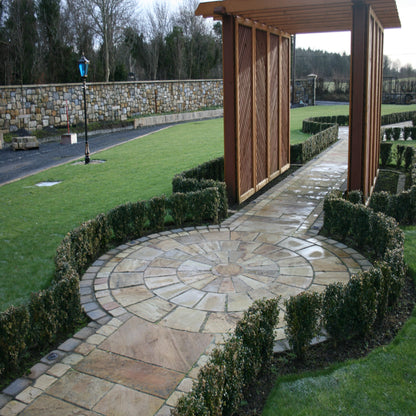 A circular pathway design completed using Tinted Mint Sandstone Paving Circle with a wooden structure and manicured hedges in the background.