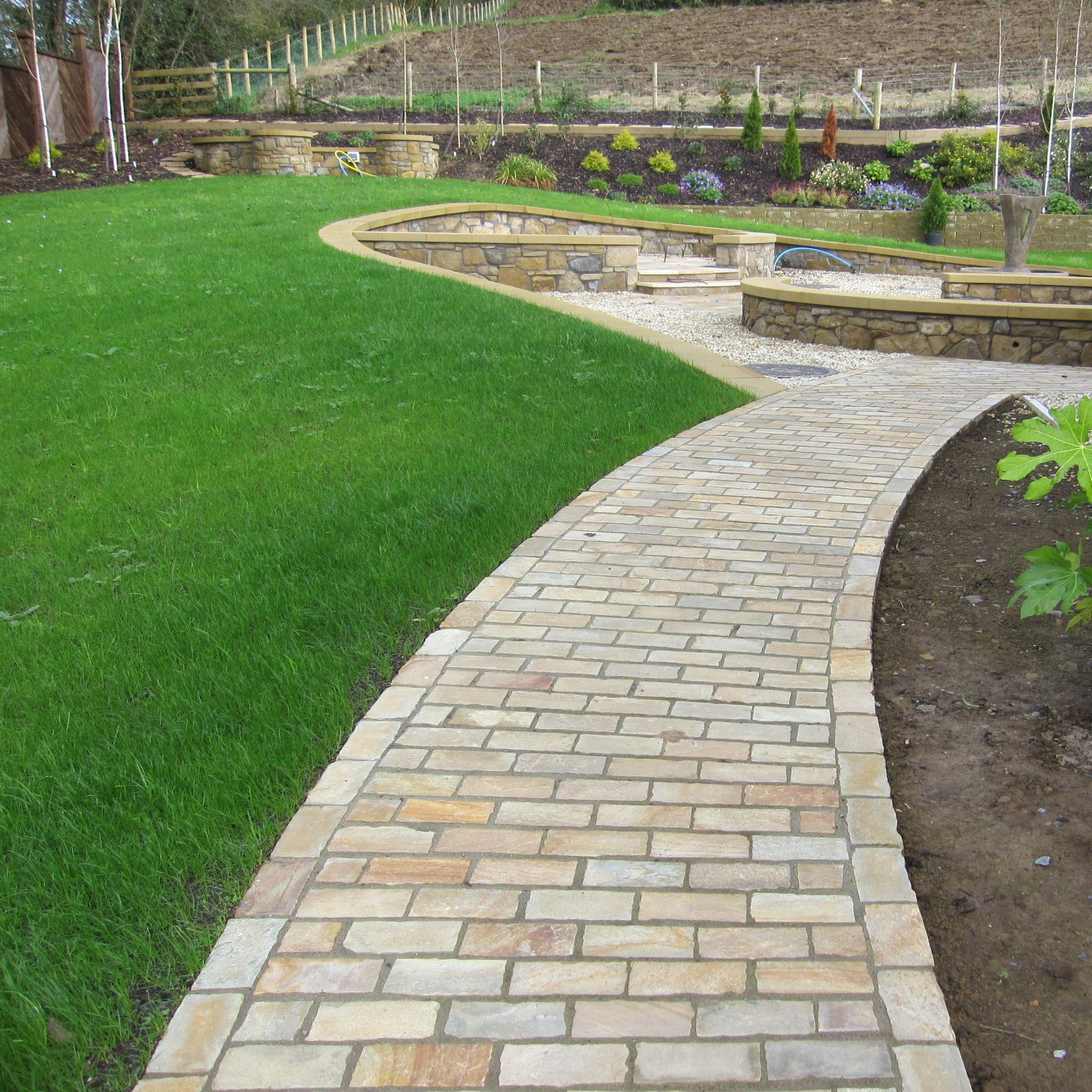 Pathway completed using Tinted Mint Sandstone Paving Setts surrounded by grass and stone walls. 