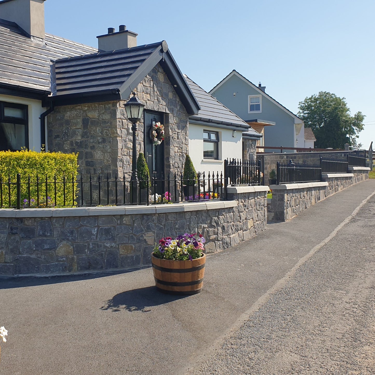 Cottage with flower pots on a sunny day. Porch and boundary wall in white limestone building stone. 