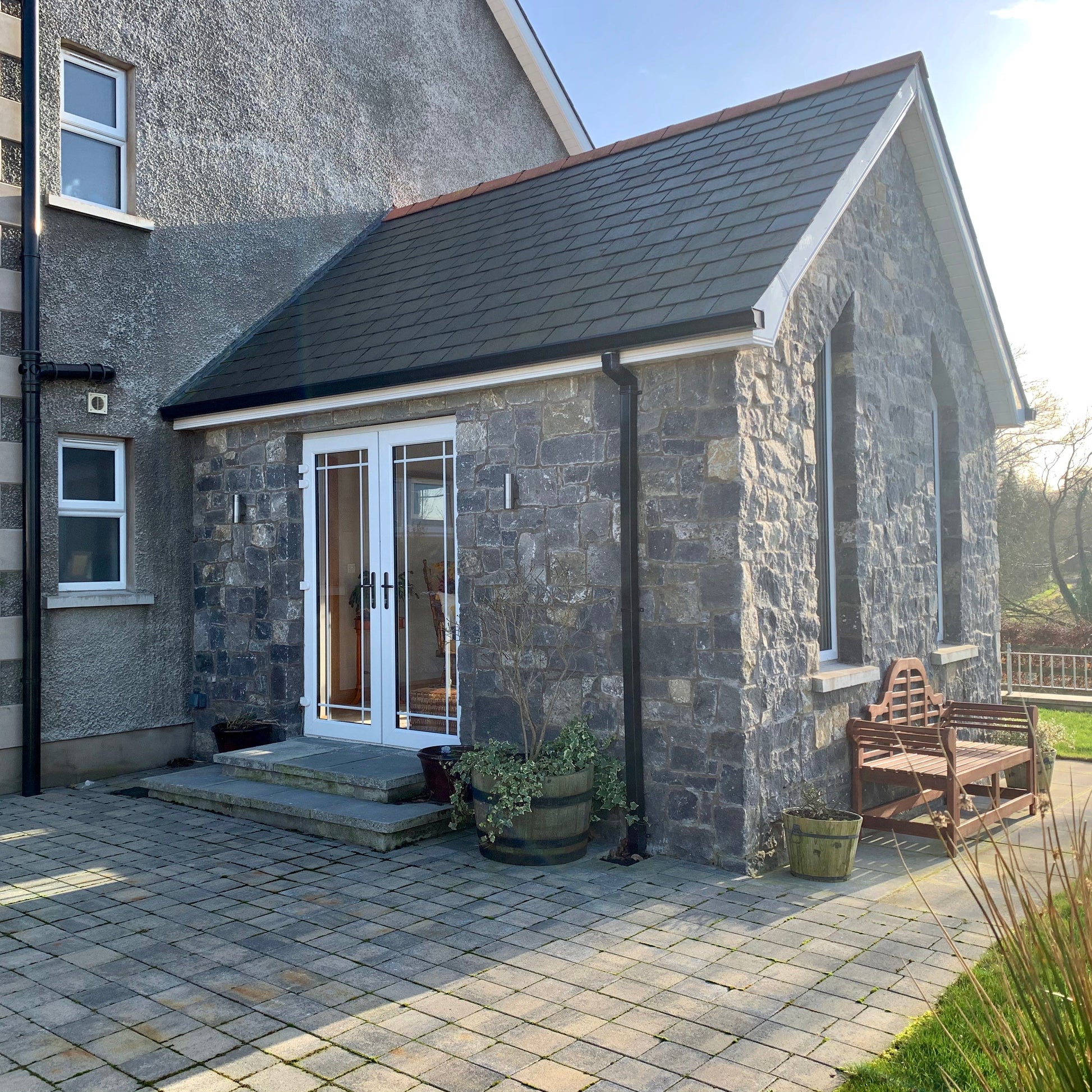 Sunroom cladded in White Limestone Stoneer Cladding looking out on to a patio area and brown bench. 