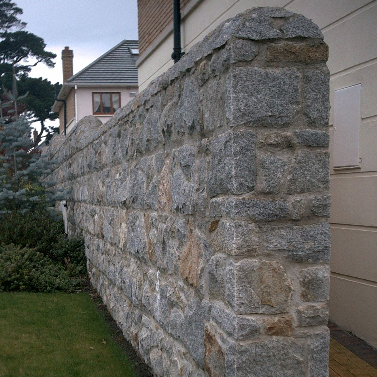 Boundary wall in Wicklow Granite machined building stone beside a residential area and surrounded by greenery. 