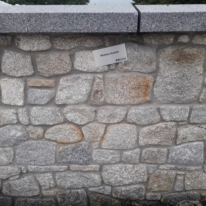 Stone wall with a label indicating material type, set against a natural background and Silver Granite wall capping.