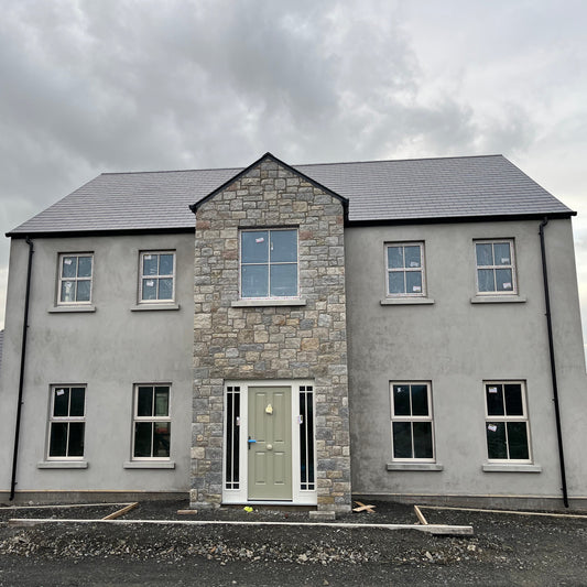 Modern house with stone façade in Wicklow Granite and grey roof under a cloudy sky