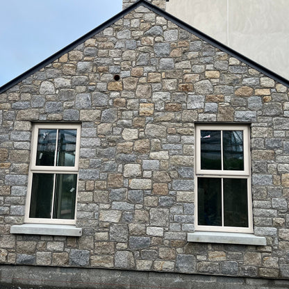 House with stone facade in Wicklow Granite and white windows against a clear sky