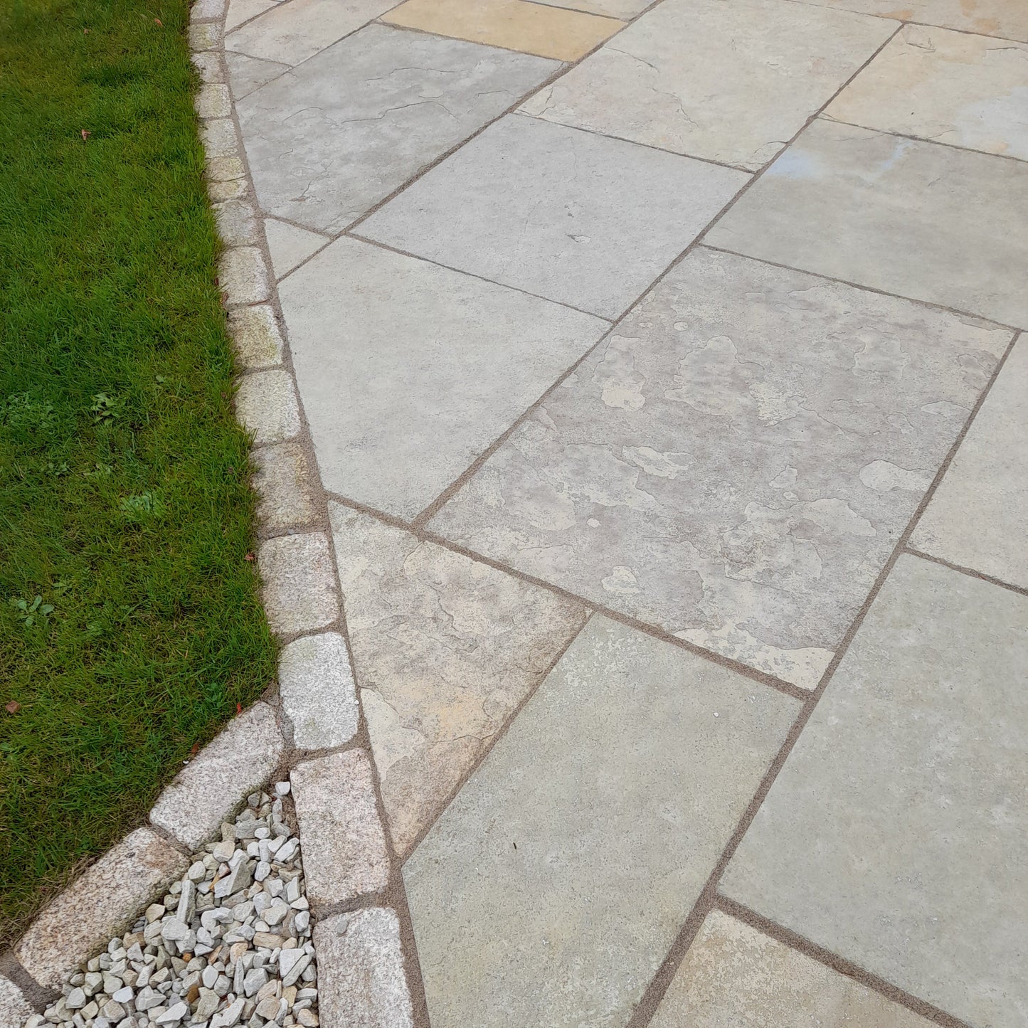 Close up of Machined Yellow Limestone Paving in patio pack format bordered by cobbles and grass. 