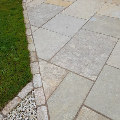 Close up of Machined Yellow Limestone Paving in patio pack format bordered by cobbles and grass. 
