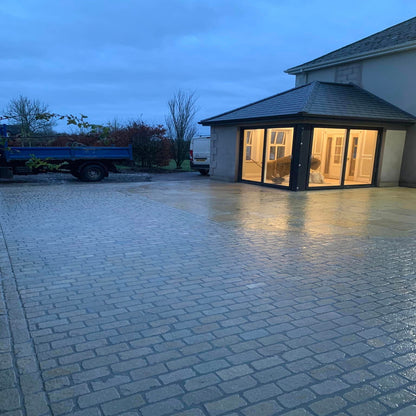 An outdoor scene featuring tumbled Yellow Limestone paving cobbles used for paving a area in front of a house, with a tractor and trees in the background.