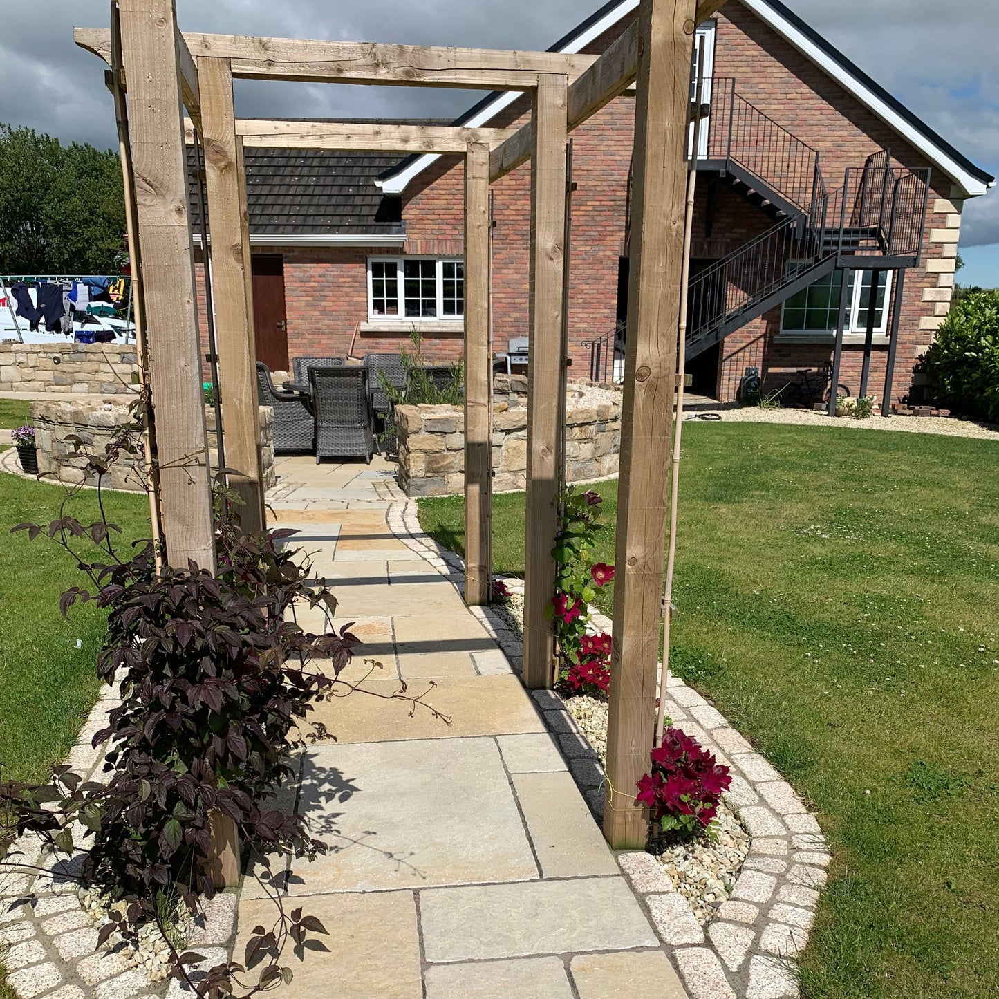 Pathway with wooden pergola leading to outdoor seating area. Paving is Yellow Limestone Tumbled Patio Packs. 