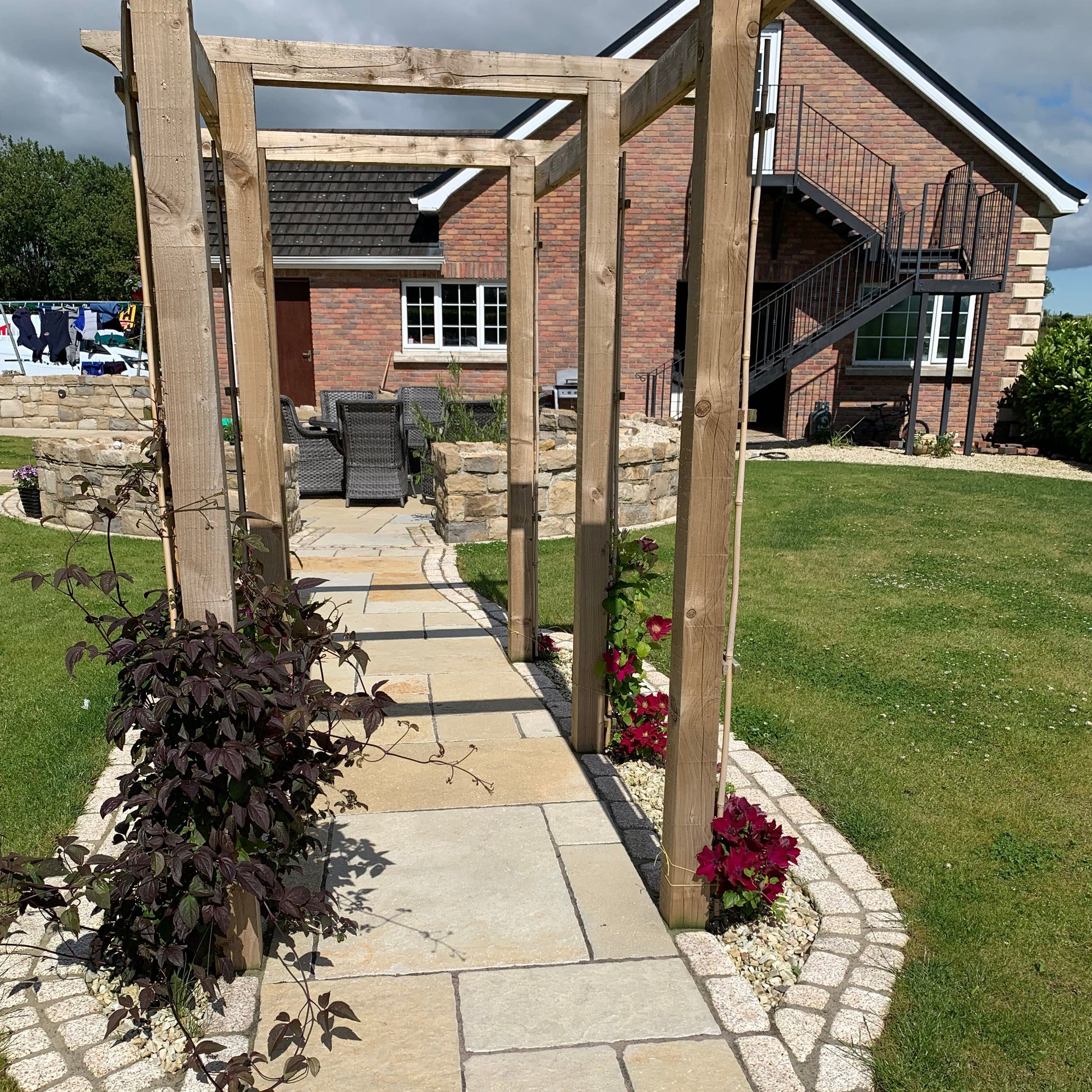Pathway with wooden pergola leading to outdoor seating area. Paving is Yellow Limestone Tumbled Patio Packs. 
