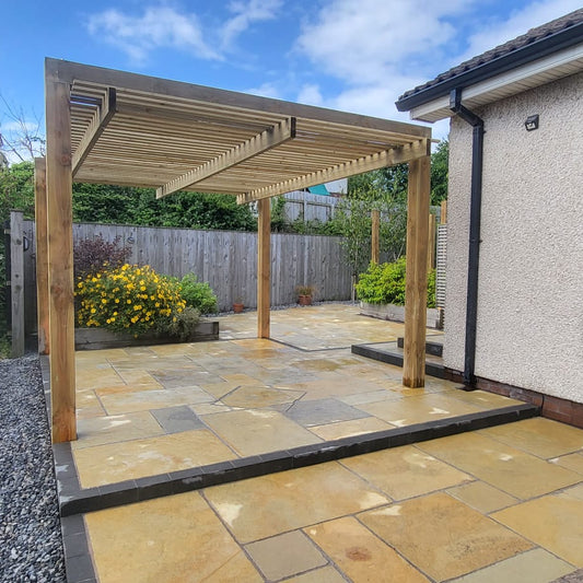 Wooden pergola over a stone patio with garden and house in the background. Paving is Yellow Limestone Tumbled Patio Packs. 